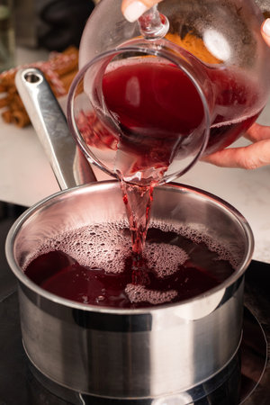 Preparation of mulled wine. A woman pours wine into a saucepan.の写真素材