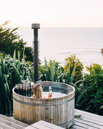Caucasian female relaxing in outdoor hot tub with ocean view and wine. Retreatの写真素材