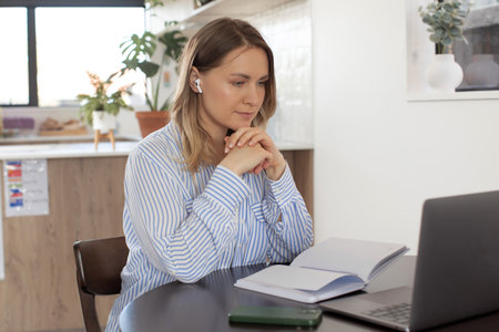Woman with wireless earphones works on laptop at tableの写真素材