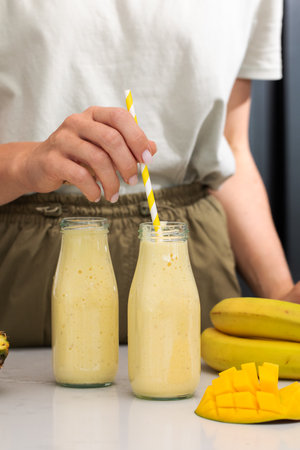 Refreshing mango banana smoothie with striped straw and fresh ingredients for detoxの写真素材