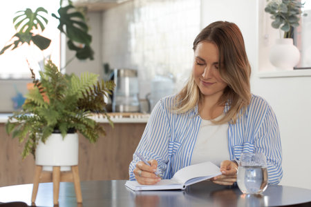 Woman writing in notebook at home with relaxed atmosphereの写真素材