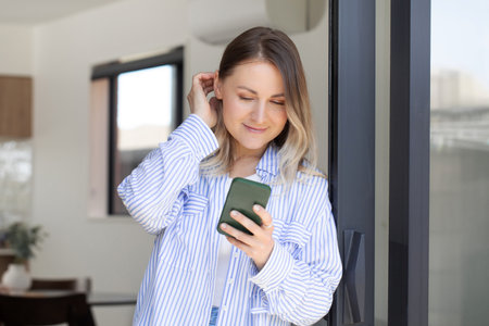 Smiling woman reads message on smartphone in terrace doorwayの写真素材