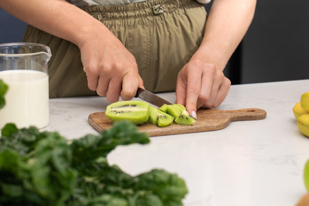 Preparing fresh kiwi slices for a healthy smoothie in a modern kitchen settingの写真素材