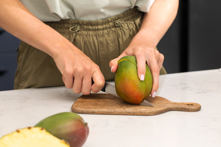Person cutting ripe mango on wooden board for fresh summer snack preparationの写真素材