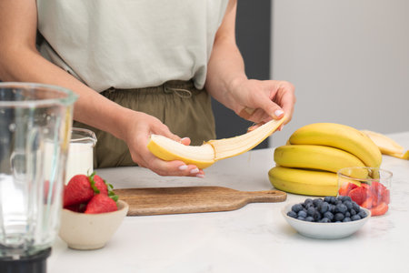Preparing fresh banana smoothie with strawberries and blueberries on a kitchen counterの写真素材