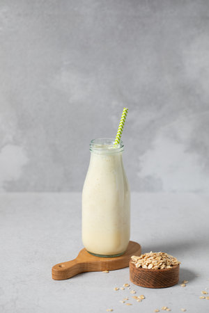 Refreshing oat milk smoothie with straw in glass bottle on gray surface. Detoxの写真素材