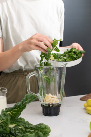 Preparing a healthy green smoothie with kale and banana on a bright kitchen counterの写真素材