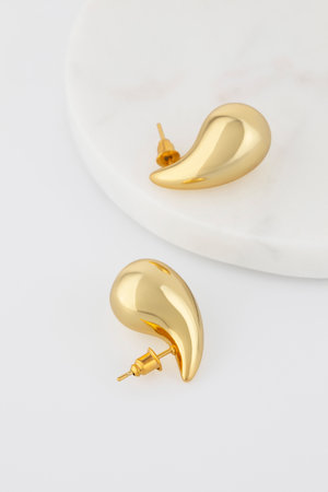 Elegant gold droplet earrings resting on marble surfaceの写真素材