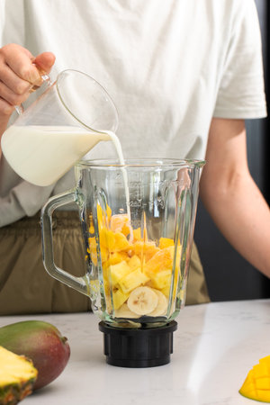 Fresh tropical smoothie preparation with mango, pineapple and milk in a modern kitchenの写真素材