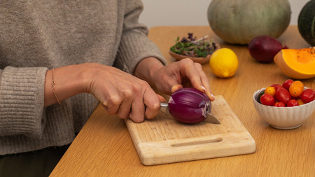 Female hands chopping red onion on wooden cutting board with fresh ingredientsの写真素材