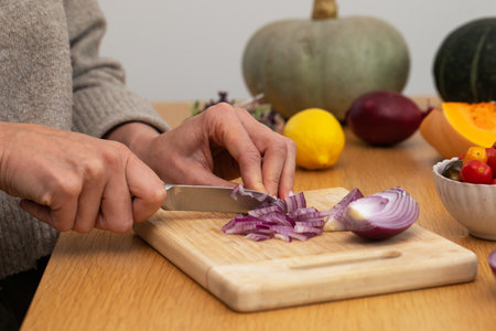 Female hands chopping red onion on wooden cutting board with fresh ingredientsの写真素材