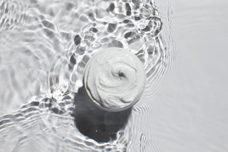 Whipped cream in rippling water for skincare design. An open jar of skin moisturizer.