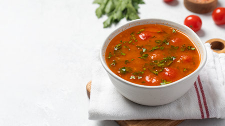 Vegetable fresh soup with tomatoes and herbs in white bowl on linen napkin. Copy spaceの写真素材