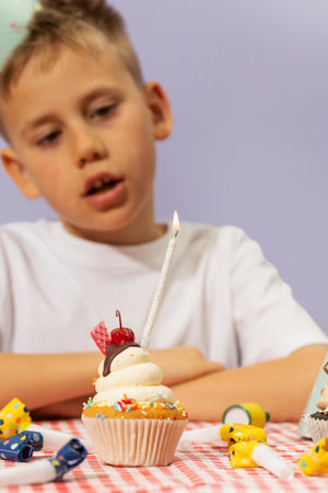 Cute boy in party hat blows out candle on birthday cupcakeの写真素材