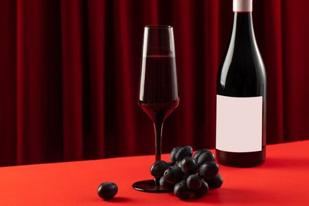 A glass of red wine and a bottle of wine with an empty label on a red background