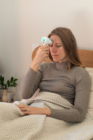 Caucasian female checking temperature with digital thermometer in bed. Respiratory infection