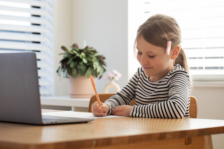 Young happy girl engaged in e-learning at home with laptop and notebook.の写真素材