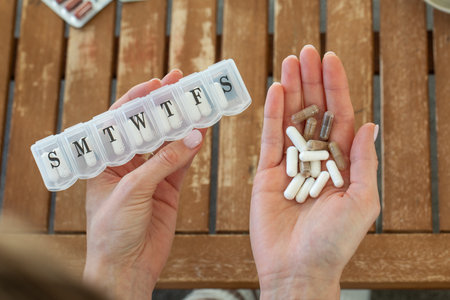 Hands holding weekly pill organizer and various supplements on wooden tableの写真素材