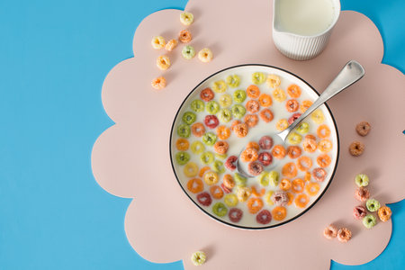 Colorful fruity cereal breakfast on pink mat with milk on blue background