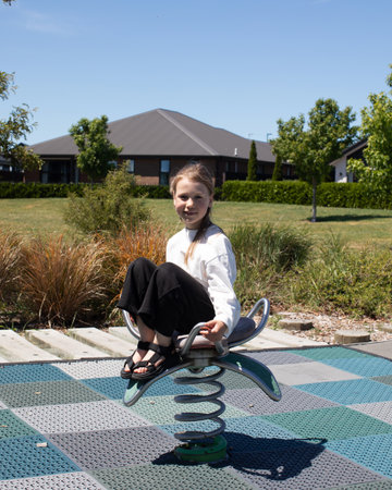 Girl sitting on spring rider at outdoor playground on sunny dayの写真素材