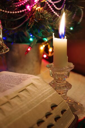 ChristmaReading the Holy Bible by candlelight near the festive lights of Christmas timeの写真素材