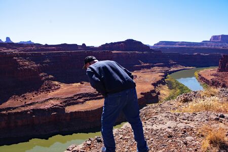 A man is looking over the edge of a cliff at the river belowの写真素材