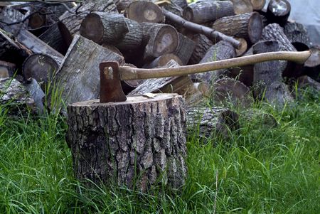 Axe splitting wood with pile of timber behind の写真素材