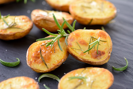 Baked unpeeled potatoes with rosemary and salt on a slateの写真素材