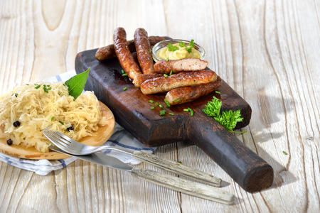 Fried Bavarian sausages from Nuremberg with mustard served on a rustic steak board with a portion of Sauerkrautの写真素材