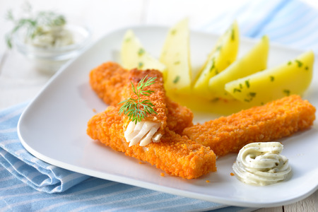 Crispy fish fingers of breaded pollack fillet served with parsley potatoes and remoulade sauce on a white plateの写真素材