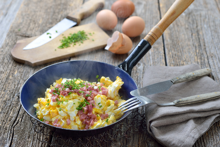 Hearty scrambled eggs with bacon and chives served hot in an old enamel frying panの写真素材
