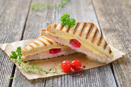 Pressed and toasted sandwich Hawaiian style with ham, pineapple and cheese served on sandwich paper on a wooden tableの写真素材