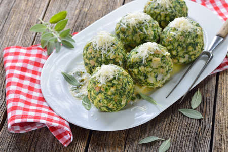 Homemade traditional South Tyrolean spinach dumplings made of white bread and fresh spinach leaves, served with melted sage butter and grated parmesan cheese on a white platterの写真素材