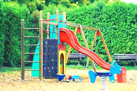 Colorful playground for kids in a sandy ground with a hedgerow in the backgroundの写真素材
