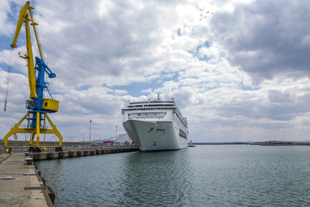 A high port crane in blue and yellow against the background of a dramatic sky and a large white shipの写真素材