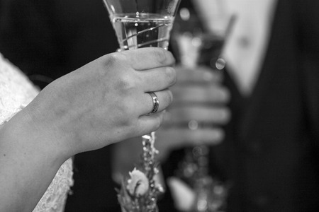 Honeymooners say cheers with champagne in black and white. grain effect. bride and groom with a glass of champagne in hand are celebrating their wedding.の写真素材