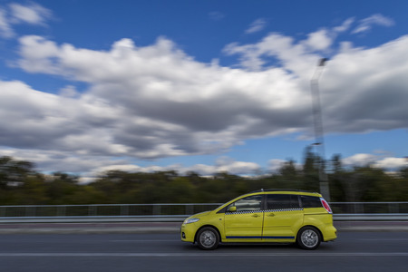 a fast moving car against the backdrop of a beautiful blue sky and fluffy white clouds. Editorial use only. Burgas, Bulgaria. 10.31.2017. light grainy effect for bigger drama and blurry effect.のeditorial素材