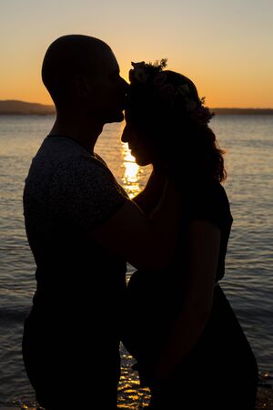 Pregnant couple on the beach at sunset. waiting for the baby.Pregnant girl posing with her husband against the background of a beautiful sunset during the blue hour.の写真素材
