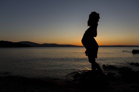 Pregnant couple on the beach at sunset. waiting for the baby.Pregnant girl posing with her husband against the background of a beautiful sunset during the blue hour.の写真素材