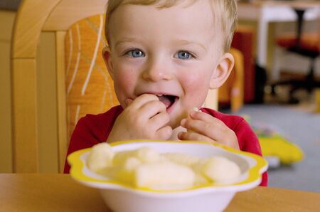 Happy toddler enjoying gluten free corn puffs in the bowl. Child concept.の写真素材