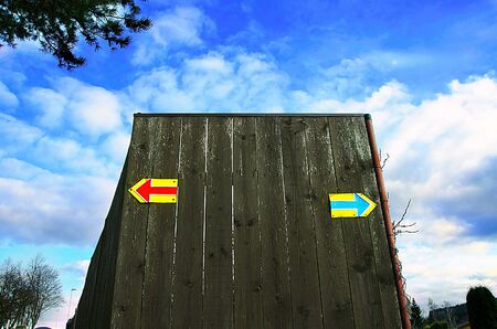 Red and blue arrows marking opposite direction of two cycling path. Yellow marks are drawn on a plank fence. Blue sky with clouds in the background.の写真素材