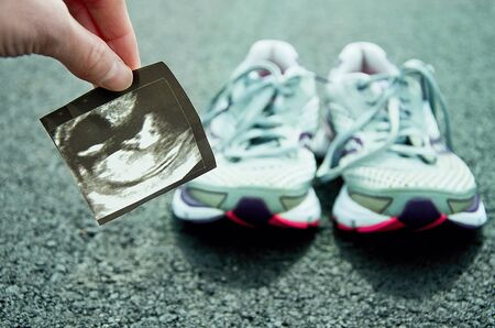 Running in pregnancy. Ultrasound image of unborn child with running shoes and road in the background.の写真素材