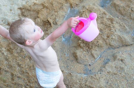 Cute toddler is playing with plastic jug on beach during summer. View from aboveの写真素材