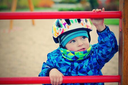 Portrait of toddler climbing a ladder during winter. He has a helmet because of safety.の写真素材