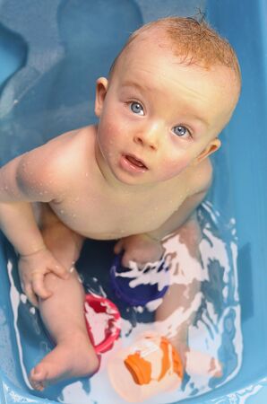 Cute boy looking at his parent during washing in a bathtub. Baby was playing with a plastic cups.の写真素材