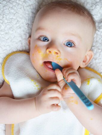 Closeup portrait of cute and dirty baby holding a spoon in his mouthの写真素材