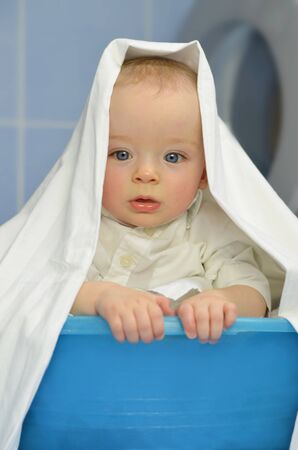 Cute baby in laundry basket in front of washing machine. Child concept.の写真素材