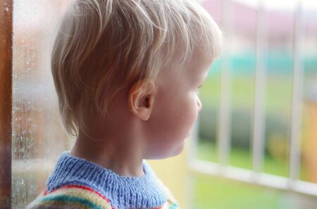 Little boy staying in opened window and watching garden in the rain.  Black and white version.の写真素材