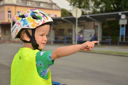 Little boy in the reflective vest pointing on the cars in the street. He is watching a traffic on the roadの写真素材