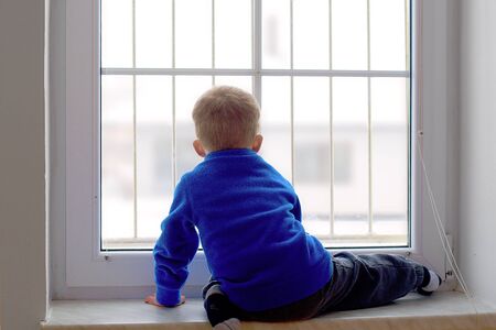 Little boy watching snowy surroundings from windowの写真素材